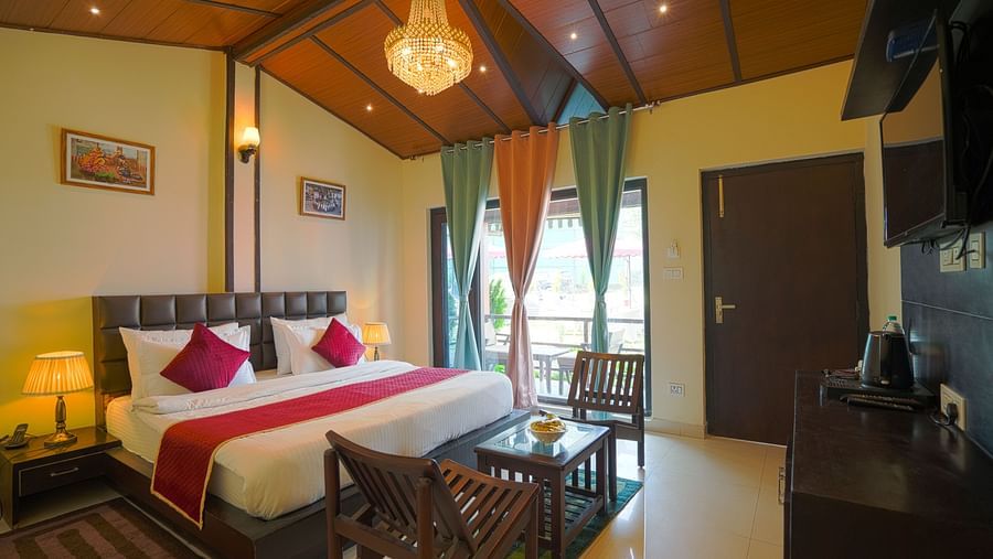A neatly arranged room with a large bedding, two coffee chairs made in wood on either side of a coffee table, chandelier etc